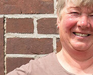 Die stolze Weiterbildungsteilnehmerin Astrid Estel steht, die Hände auf die Hüften gestützt, vor einer geziegelten Hauswand.