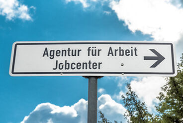 ein weißes Straßenschild auf dem "Agentur für Arbeit Jobcenter" steht