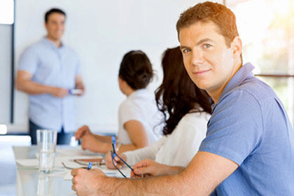 ein Mann sitzt an einem Tisch mit einem Laptop in einem Klassenraum